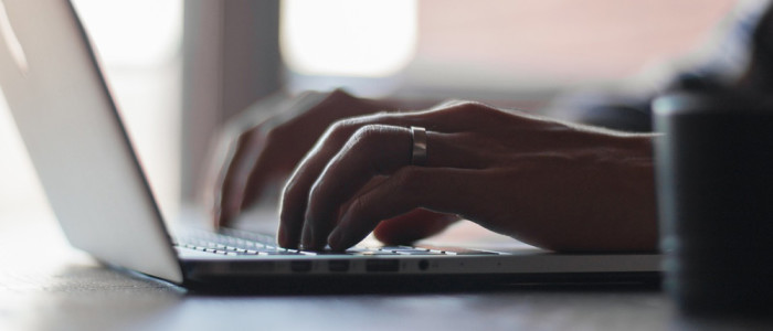 Two hands typing on a laptop keyboard, window in the background.